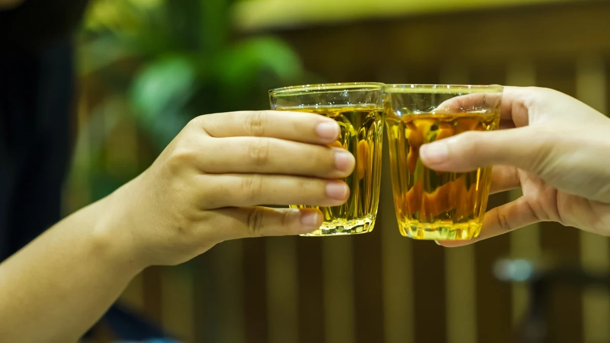 Duas mãos brindando com copos de cachaça
