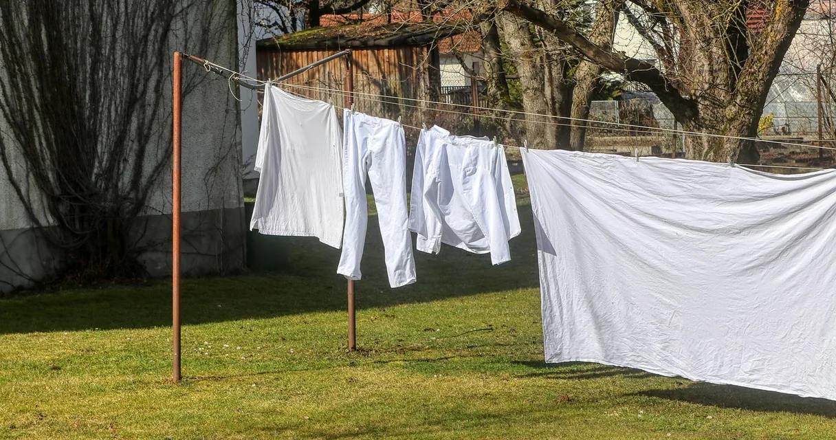 Camisas e calças brancas de trabalho secando no varal de um quintal